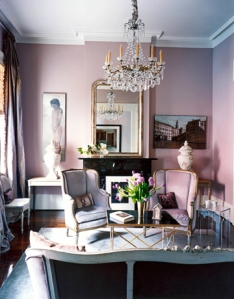 pink-walled room with white ceiling, crystal chandelier, 2 small chairs and small settee, mirror over black marble fireplace,
