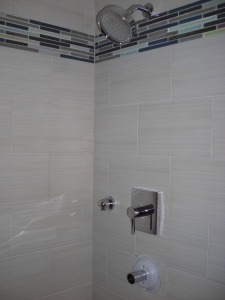 Shower with porcelain tile, Kohler showerhead and faucet, band of glass tile below showerhead